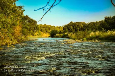 a river with rocks and trees in the background at Cabañas El Cardón in Santa Rosa de Calamuchita