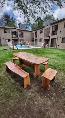 a wooden picnic table and two benches in a yard at Departamento con pileta y asadores in Villa General Belgrano