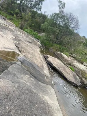 a river with rocks next to a hill with trees at Apart La Sole in Tanti