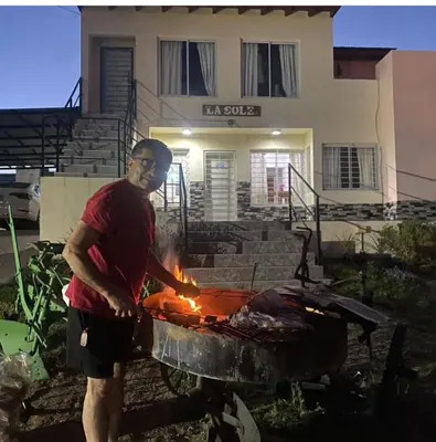 a man cooking food on a grill in front of a house at Apart La Sole in Tanti