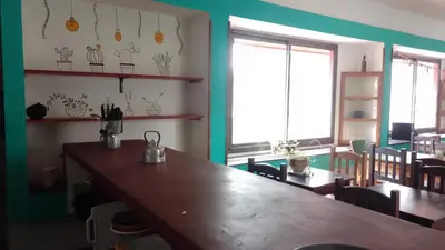 a dining room with a wooden table and some windows at La Brújula Hostel y Club Social in Mina Clavero