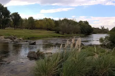 a river with rocks and grass next to a field at Loft Campestre - Los Reartes in Los Reartes
