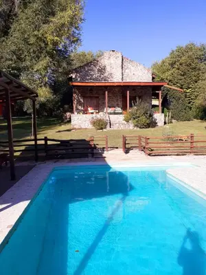 a swimming pool in front of a stone house at Refugio de las Sierras in Villa General Belgrano