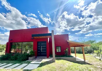 a red house with a blue sky and clouds at Refugio Serrano in Merlo