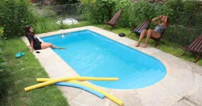 two women are sitting next to a swimming pool at Cabañas La Petunia in Santa Rosa de Calamuchita