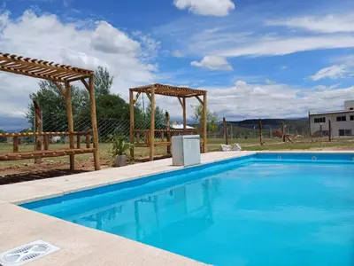a blue swimming pool with a wooden pergola at Cima Capri Cabañas in Villa Carlos Paz