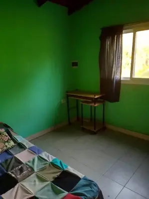 a green room with a table and a bed and a window at Casa con gran jardín a 100 mts del Río Amboy in Villa Amancay