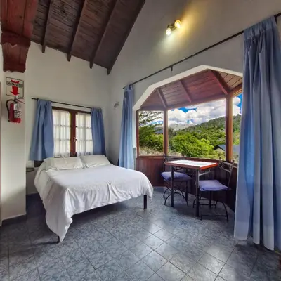 a bedroom with a bed and a table and a window at Cabañas Cerro Cristal in La Cumbrecita