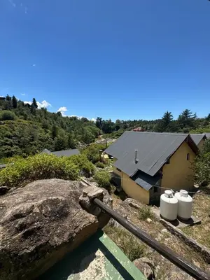 a house with a slate roof and two white buckets at Cabañas Cerro Cristal in La Cumbrecita
