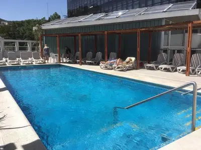 a large blue swimming pool with people sitting in chairs around it at Amérian Carlos Paz Depto Particular 108 in Villa Carlos Paz