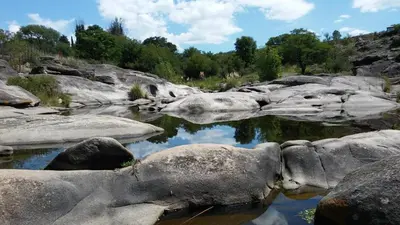 a river with rocks and trees in the background at Cabaña en Punilla in Villa Parque Siquiman