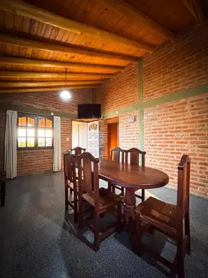 a wooden table and chairs in a room with a brick wall at Cabañas Altos del Tintero in Mina Clavero
