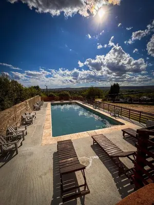 a swimming pool with wooden benches and chairs on a patio at Cabañas Altos del Tintero in Mina Clavero