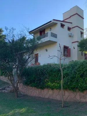 a large white house behind a stone wall at Hermosa casa de veraneo con pileta in Villa Carlos Paz