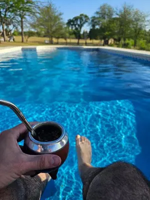 a person holding a cup of coffee next to a swimming pool at Complejo de cabañas- Lomas del Sol in Los Reartes