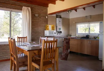 a kitchen with a wooden table and chairs and a table and a counter at Complejo de cabañas- Lomas del Sol in Los Reartes