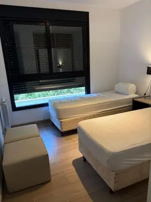 two beds in a room with a window and a chair at Complejo Las Pircas Alta Gracia in Alta Gracia
