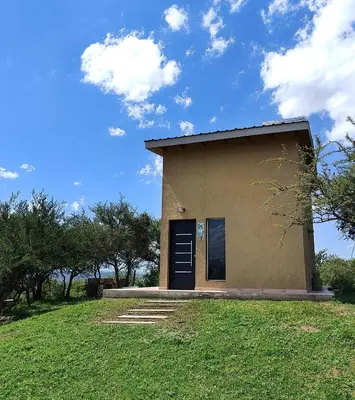 a small building with a blue door on a grass field at Complejo MASVISTA in San Antonio de Arredondo
