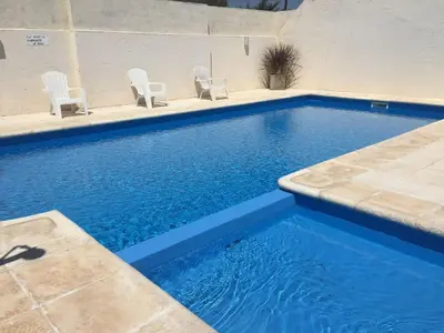 a swimming pool with white chairs and blue water at Hosteria Torol Calta in Villa Cura Brochero