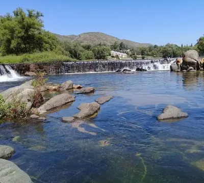 a river with rocks in front of a waterfall at Campamento Monarcas in Villa Carlos Paz