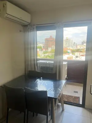 a dining room table with chairs and a large window at Dpto con piscina , asador & terraza in Villa Carlos Paz