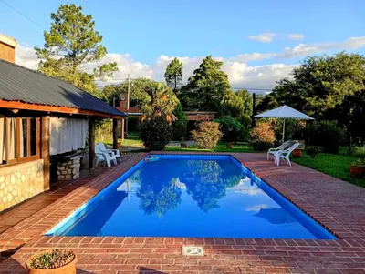a swimming pool in a yard with two chairs and an umbrella at Refugio Verde en Nono, Córdoba in Nono