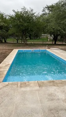 a large blue swimming pool with trees in the background at Cabañas Valle de Anisacate 4 in Villa Anizacate