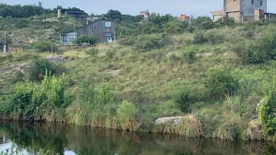 a grassy hill next to a body of water at La Roca in Estancia Vieja