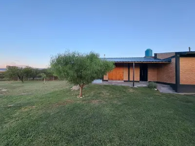 a house with a tree in front of a yard at Los Chivos in Villa Cura Brochero