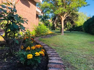 a garden with flowers next to a brick building at Casa frente al rio San Antonio Playas de Oro Villa Carlos Paz in Villa Carlos Paz