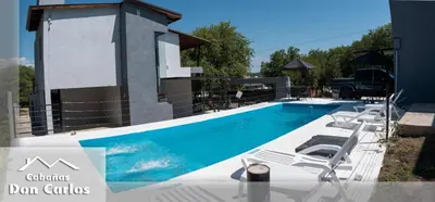 a swimming pool with lounge chairs next to a house at Cabañas Don Carlos in Villa Carlos Paz