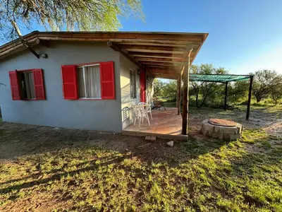 a small white house with red shutters and a deck at El Ashva casa de campo y santuario de caballos in Las Calles