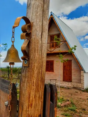 an old bell on a wooden pole with a house at Cabañas Alpinas M y M in Bialet Massé
