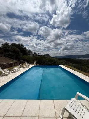 a large swimming pool with chairs and a sky with clouds at Chalet de montaña in Villa Carlos Paz