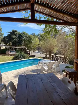 a wooden table and chairs next to a swimming pool at Departamento frente al rio solo familias in Villa Carlos Paz