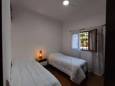 a white bedroom with two beds and a window at Casa con pileta cómoda y equipada in Villa Carlos Paz