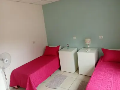 two beds in a room with pink sheets and a fan at Hostel El Chinchero in Merlo
