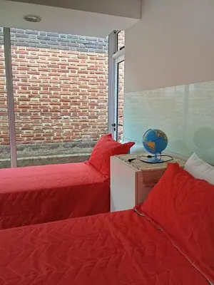 two beds with red sheets in a room with a window at Hostel El Chinchero in Merlo