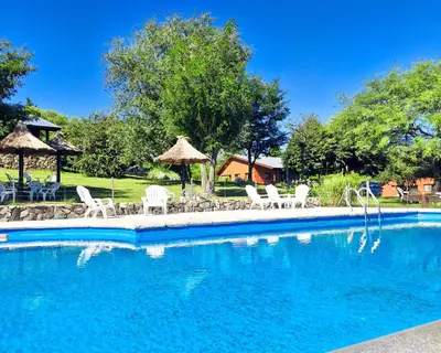 a swimming pool with white chairs and umbrellas at Cabañas Balcon al Champaqui in Villa General Belgrano