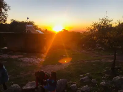 a group of people sitting in a field at sunset at Puesto Kupuka in Villa de Las Rosas