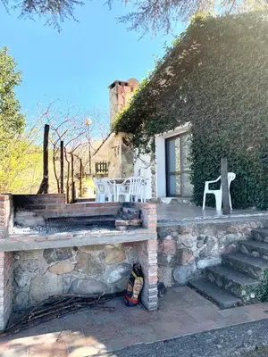 a stone house with two white chairs and a porch at casa vista al lago in Villa Carlos Paz