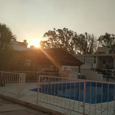 a pool in front of a house with the sun setting at Santa Rita Dpto in Villa Carlos Paz