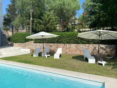 two umbrellas and chairs next to a swimming pool at Altos del Oeste in Villa Carlos Paz