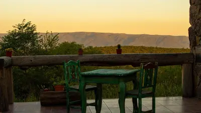 a table and chairs sitting on a porch with the sunset at Merlín Art Lodge in Atos Pampa