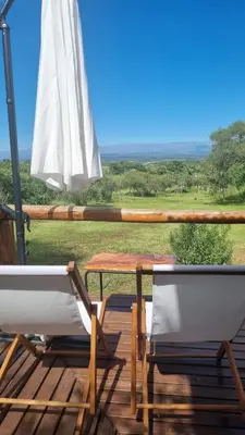 two chairs and a table and an umbrella on a deck at Cabaña Cielos del Champaqui 6 kms VGB in Villa Ciudad Parque