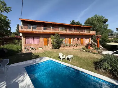 a house with a swimming pool in front of a building at Cabaña frente al rio solo familias in Villa Carlos Paz