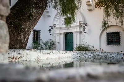 a white building with a green door and a tree at Hotel El Potrerillo de Larreta in Alta Gracia