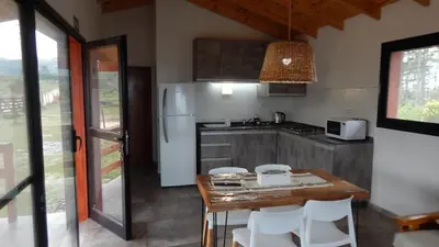 a kitchen with a table and chairs and a refrigerator at Cabañas Aldea Lucerna La Cumbrecita in La Cumbrecita