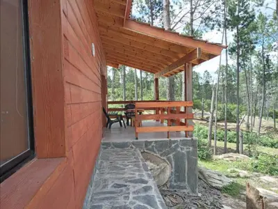 a porch of a wooden cabin with a table and bench at Cabañas Aldea Lucerna La Cumbrecita in La Cumbrecita