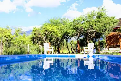 a swimming pool with two white chairs and trees at Amaneciendo cabañas in Merlo